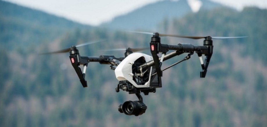 Bild einer Drohne, die in einer bergigen, mit Wald bewachsenen Landschaft fliegt.